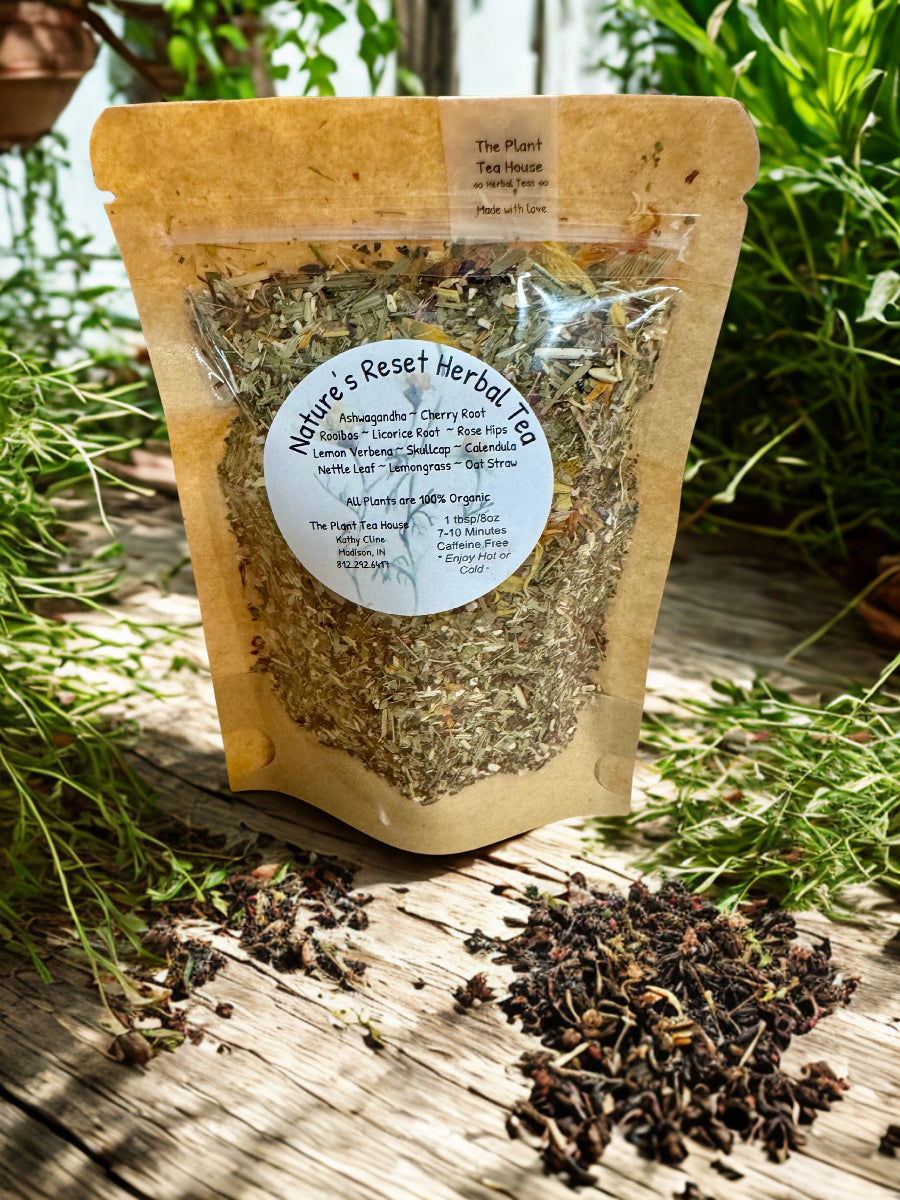 Herbal tea package with loose tea leaves on a wooden surface with greenery in the background